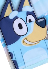 Tissu en polyester bleu présentant un personnage de chien en cartoon avec de grands yeux, un visage bleu clair et un corps bleu foncé, rehaussé de détails jaunes.