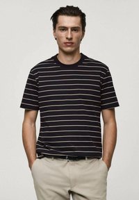 Marinrandig t-shirt med krämfärgade linjer, korta ärmar och standard rundad hals. Bärs med ljusa byxor som visar en avslappnad passform.