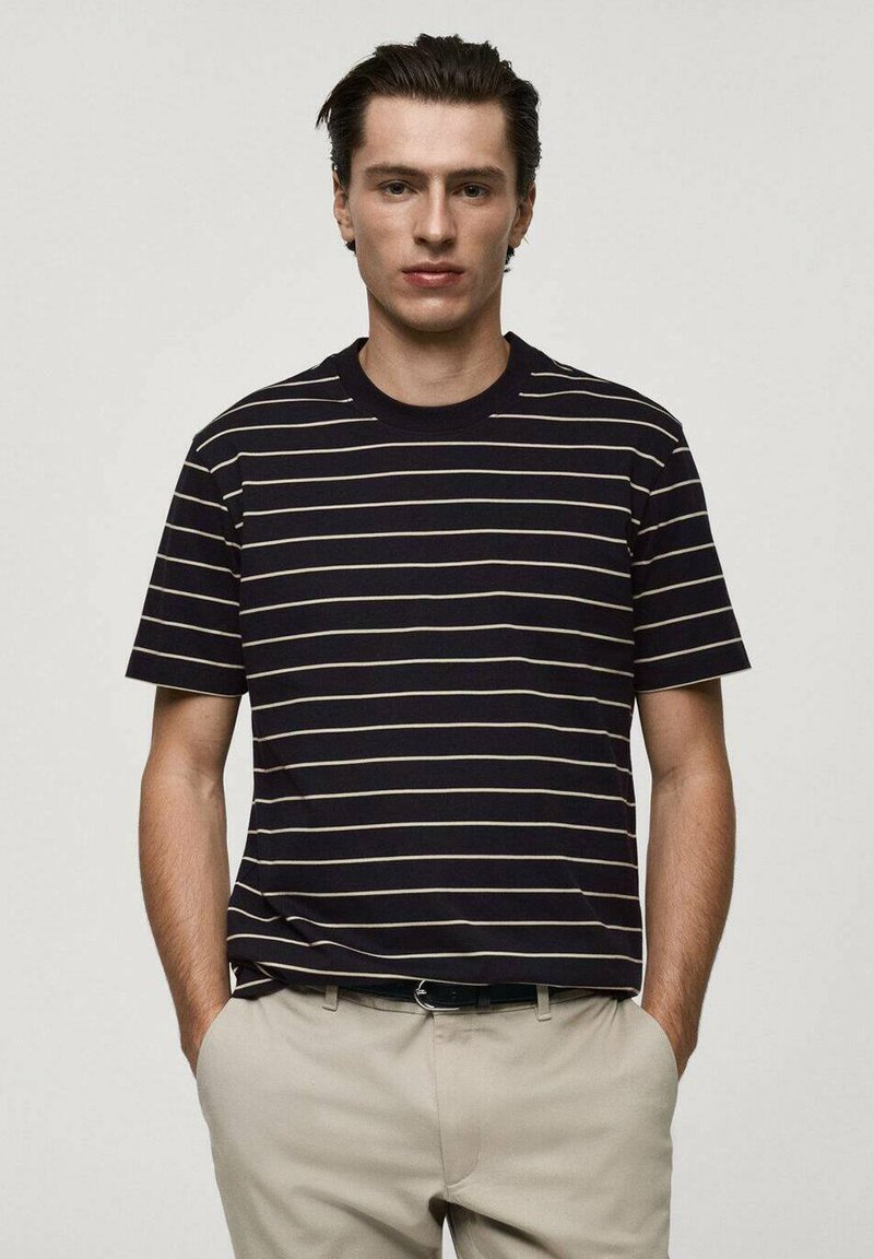 Marinrandig t-shirt med krämfärgade linjer, korta ärmar och standard rundad hals. Bärs med ljusa byxor som visar en avslappnad passform.