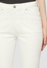 Jeans in denim bianco con un design aderente, stile a cinque tasche, accessori in argento sui bottoni e tasche, e una texture liscia.