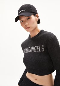 Jersey corto negro con el texto "ARMEDANGELS" en gris, que presenta un cuello redondo. Además, hay una gorra negra con "PERMANENT" bordado en blanco.