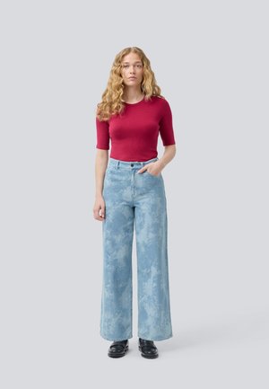 Red ribbed short-sleeve top and light blue wide-leg jeans with a marbled pattern, paired with black shoes. Model stands with one hand in pocket.