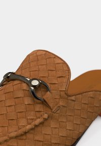 Καφέ πλεκτό δερμάτινο μοκασίνι με ασημένια λεπτομέρεια με σχέδιο αλόγου στην κορυφή και πλεκτή δερμάτινη επένδυση.