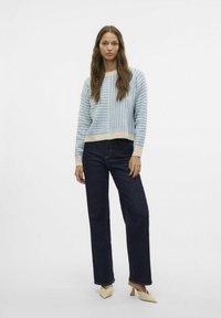 Maglione a righe blu e crema con scollo rotondo, abbinato a jeans dritti scuri e scarpe color crema. Texture a maglia liscia.