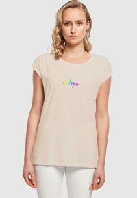 Helles beiges T-Shirt aus weichem Stoff, mit kurzen umgeschlagenen Ärmeln und einem bunten "#Hope"-Grafik auf der Vorderseite.