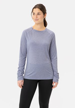 Langere mouw sporttop in lichtblauwe stof met een gladde textuur, ronde hals en duimgaten bij de manchetten. Gepaard met zwarte legging.