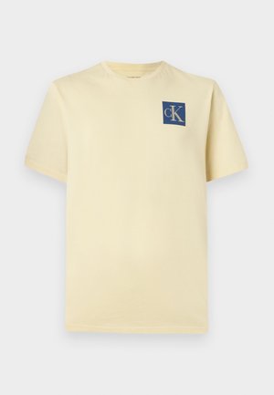 Žuta pamučna majica kratkih rukava s plavim kvadratnim logotipom "cK" na lijevoj strani prsnog dijela. Klasičan dizajn s okruglim izrezom.