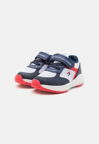 Scarpe sportive con una parte superiore in mesh bianco traspirante, dettagli in navy e rosso, cinturino regolabile e suola in gomma testurizzata.