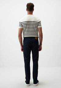 Dwukolorowa, w paski, koszulka dzianinowa z krótkim rękawem w kolorze kremowym i granatowym, zestawiona z ciemnoniebieskimi spodniami slim-fit. Buty są białe z teksturowanym wykończeniem.