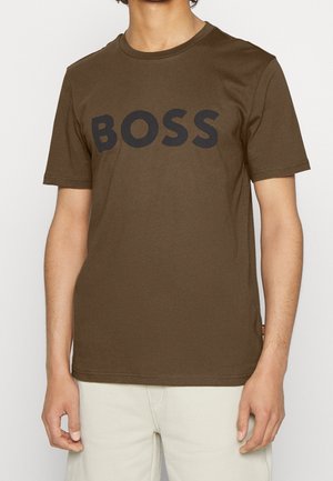 Person trägt ein olivgrünes T-Shirt mit kurzen Ärmeln mit dem Wort "BOSS" in großen schwarzen Buchstaben auf der Brust.