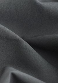 Gros plan sur un tissu gris foncé avec une texture fine tissée et des plis doux créant des ombres douces.