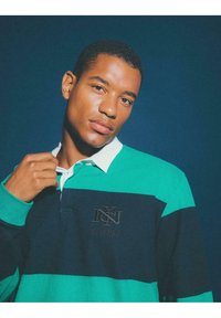 Polo w paski w odcieniach zieleni i granatu z białym kołnierzykiem, z haftowanym logo na piersi i długimi rękawami. Gładka tekstura.