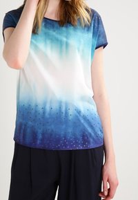 Blusa de manga corta, con un degradado de blanco a azul, presenta una tela suave con un estampado de puntos cerca del dobladillo. Ribete en color marino en el escote y las mangas.