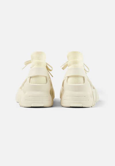 Jasnokremowe buty sportowe z plecionym wierzchem, gumową podeszwą i sznurowadłami. Posiadają uchwyty i teksturowane wzory na podeszwie.