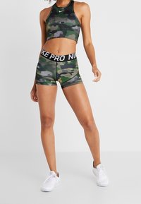 Camo-patterned sports bra and shorts set in green and black. Bra has a high neckline; shorts feature a black Nike Pro waistband.