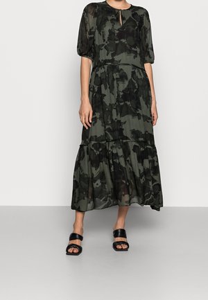 Maxikleid in Dunkelgrün mit floralem Muster, mit rundem Ausschnitt, kurzen Puffärmeln und gestuftem Rock. Wird mit schwarzen Sandalen kombiniert.