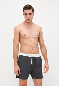 Bañadores grises con cintura con cordón blanco, bolsillos laterales y detalles laterales en blanco, fabricados en un material ligero y de secado rápido.