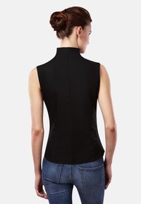 Top noir sans manches avec col montant, design ajusté et texture lisse. Porté avec un jean en denim bleu, mettant en valeur une silhouette ajustée au dos.