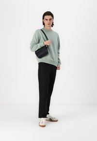Hanorac verde mentă, pantaloni negri, adidași albi cu accente maro și o mică geantă crossbody neagră. Design simplu, modern.