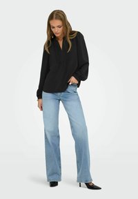 Svart långärmad topp med en veckad frontdesign. Matchad med ljusblå högmidjade utsvängda jeans och svarta spetsiga klackar.