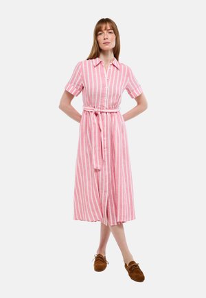 Femme portant une robe rayée verticale rose et blanche longueur genou avec manches courtes et ceinture nouée à la taille, associée à des chaussures marron à lacets.