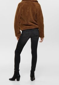 Brun, fluffig fleecejacka med krage, matchad med svarta, slim-fit jeans och ankelskorts med en texturerad yta och staplad klack.