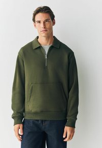 Olivgrüner Pullover mit Viertel-Reißverschluss, vordertasche im Känguru-Stil und gerippten Bündchen. Weicher Stoff und lässige Passform.