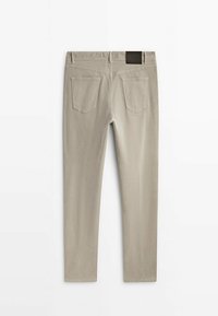 Pantalon beige slim fit vu de dos avec deux poches arrière et un patch de marque en cuir noir sur la ceinture.