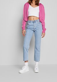 Kort rosa hoodie, vit V-ringad topp, ljusblå raka jeans och vita sneakers. Slät textur, avslappnad design och figurnära passform.