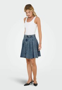 Jupe en denim au design plissé, longueur mi-cuisse, taille haute et passants de ceinture, associée à un débardeur blanc ajusté et des chaussures à talons slingback noires.
