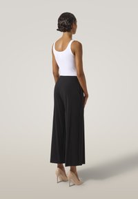 Svarta vida byxor med sidofickor, kombinerade med en vit linne och nakna högklackade skor. Slät tyg och skräddarsydd passform.