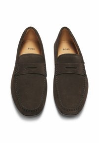 Mocasines de ante marrón oscuro con una costura elevada y puntera afilada. Forro interior suave, con un sutil branding en la plantilla.