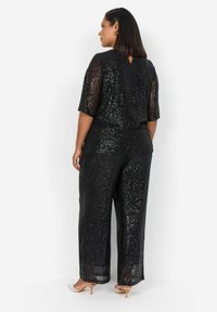 Svart paljett jumpsuit med korta ärmar, vida ben och en nyckelhålsdetalj på ryggen. Slät textur med en glänsande finish.