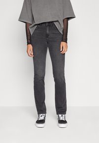 Jeans de mezclilla negra con un corte recto, que presentan una cintura de altura media. Combinados con una camiseta gris de gran tamaño y deportivas negras.