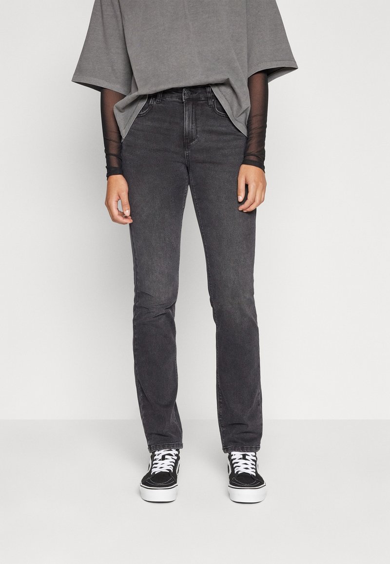 Jeans de mezclilla negra con un corte recto, que presentan una cintura de altura media. Combinados con una camiseta gris de gran tamaño y deportivas negras.