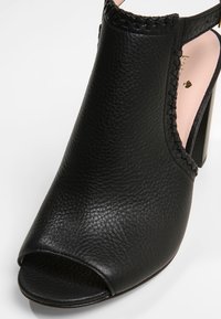 Černé kožené boty na vysokém podpatku s otevřenou špičkou, texturovaným povrchem, výřezem po stranách a tkaným detailem kolem kotníku. Růžová podšívka.