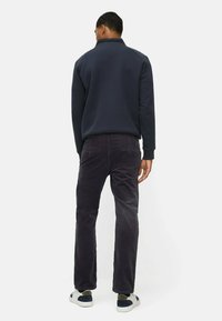 Marineblauwe gewatteerde jas met hoge kraag, gecombineerd met donkerpaarse corduroy broek en witte sneakers met blauwe en groene accenten, bekeken van achteren.
