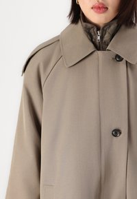 Abrigo beis con un amplio cuello, cierre frontal de botones y forro interior texturizado. Presenta botones grandes y un ajuste relajado.