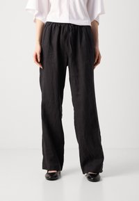 Zwarte linnen broek met een relaxte pasvorm, een elastische tailleband en een trekkoorddetail. Soepele textuur met een licht kreukelige uitstraling.