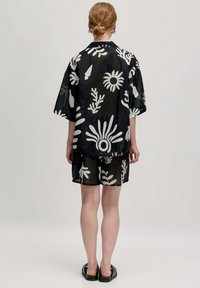 Schwarzes, durchsichtiges Shirt-und-Shorts-Set mit weißen Blumenmustern. Lässiger Schnitt mit kurzen Ärmeln und Kragen. Glatte Textur.
