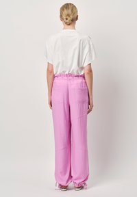 Roze losse broek met elastische tailleband en gatherings bij de enkels, gecombineerd met een witte T-shirt met korte mouwen en een ontspannen pasvorm.