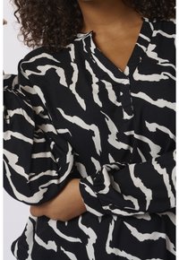 Blouse noire avec un motif abstrait blanc, décolleté en V et manches bouffantes, fabriquée à partir d'un tissu doux et léger.
