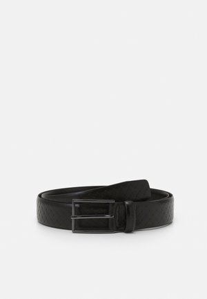 Zwarte leren riem met een geweven patroon en een rechthoekige zilverkleurige metalen gesp, opgerold op een witte achtergrond.