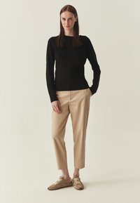 Pull noir à manches longues, pantalon beige ajusté, et baskets en suède marron avec des lacets clairs. Textures lisses, coupe ajustée.