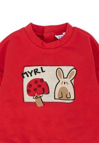 Czerwona bluza z kapturem z haftowanym wzorem grzyba z czerwonymi kropkami i beżowym królikiem, otoczona prostokątną naszywką z napisem „MYRL.”