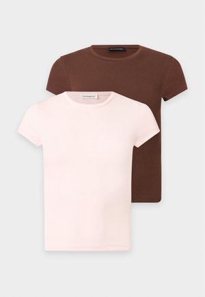 Ung kvinde smilende, iført en brun kort top, lyse denim Bermuda-shorts, hvide sokker, brune sneakers og holder en lille grøn håndtaske.