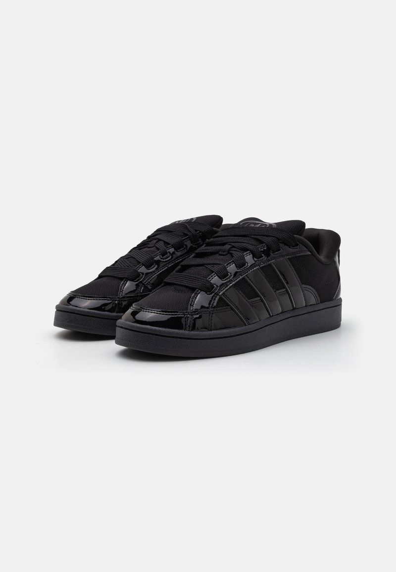 Zapatillas negras con un diseño elegante, que presentan una mezcla de materiales lisos y texturizados, cordones prominentes y acentos a rayas en los laterales.