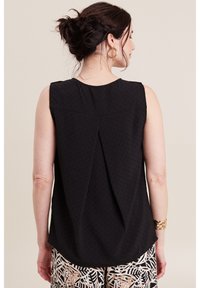 Top nero senza maniche con una texture sottile, caratterizzato da una piega sul retro, orlo curvo, indossato con pantaloni fantasia.