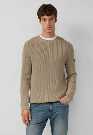 Beiger ribbed Strickpullover mit Rundhals, langen Ärmeln und einem kontrastierenden weißen Innenkragen. Mit kleinem Logo am linken Arm.