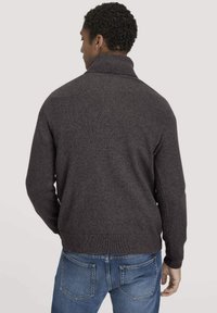 Knitpullover in Anthrazit mit hohem Kragen, gerippten Bündchen und Saum, getragen über blauen Jeans. Weicher Stoff und lockere Passform.